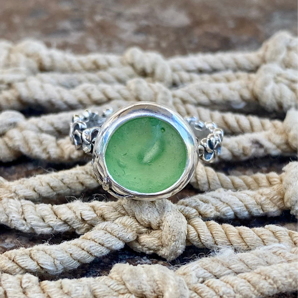 A silver ring with a bubbled round green sea glass canochon, resting on a bed of thick beige rope.